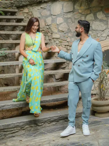 The groom gently leads his bride down a stone staircase. This candid shot captures their easy chemistry and stylish outfits, blending modern fashion with a rustic, natural setting.