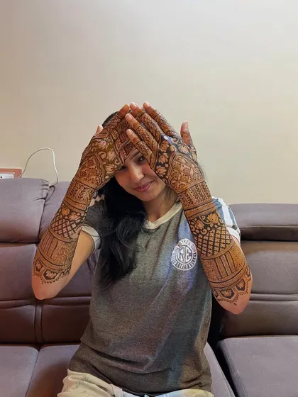 The classic face-hiding pose, which perfectly showcases the detailed mehendi on both hands.