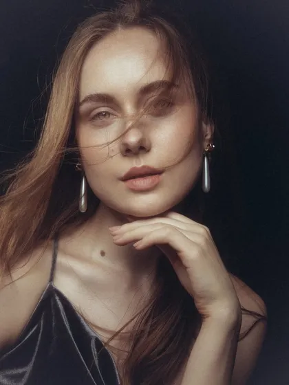 A soft and dreamy beauty portrait. The makeup is minimal, with a focus on a healthy flush on the cheeks and a natural lip tint. The wind-swept hair adds a touch of effortless movement.