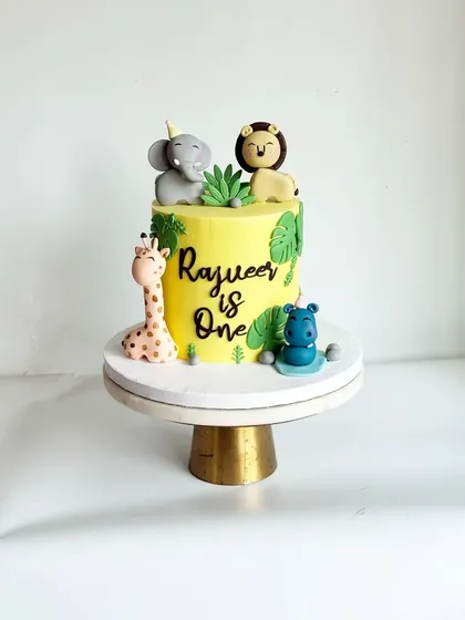 This intimate jungle-themed cake was perfect for Rajveer's first birthday. It features cute, handcrafted fondant animals like an elephant, lion, giraffe, and hippo on a vibrant yellow ganache cake.