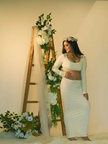 A joyful and radiant portrait. Wearing a delicate flower crown, the mother-to-be smiles, her happiness lighting up this beautiful studio shot.