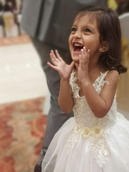 The sheer excitement of being part of a wedding. This little girl's joy is infectious as she wears her custom white gown with intricate floral lace details on the bodice and waist.