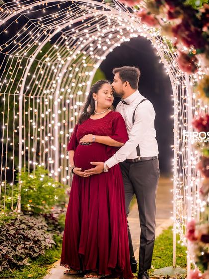 A tender moment during a maternity shoot, with the father-to-be kissing his partner's forehead under the romantic glow of the light arch.