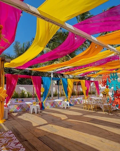 A vibrant Haldi setup with a canopy of colourful drapes and quirky chandeliers, perfect for a beachside celebration.