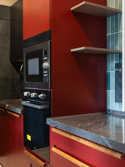 Another angle of the Marsala red kitchen, showing the integrated oven and microwave tower. The deep red is balanced by the cool tones of the blue-green tiles and the dark countertop, creating a rich and layered palette.