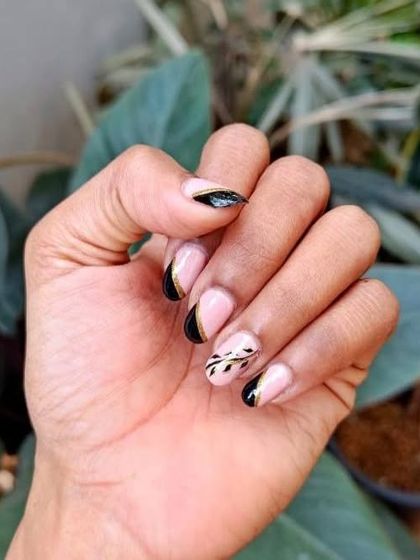A closer look at the delicate, hand-painted leaf design on these nude and black French-style nails. The gold chrome adds a touch of luxury.