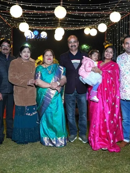 A large family group poses for a photo at an outdoor 60th birthday celebration in the evening.