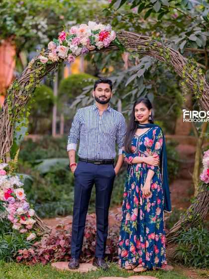 A couple poses in front of a rustic floral arch made of woven branches, a beautiful and natural frame for a romantic portrait.