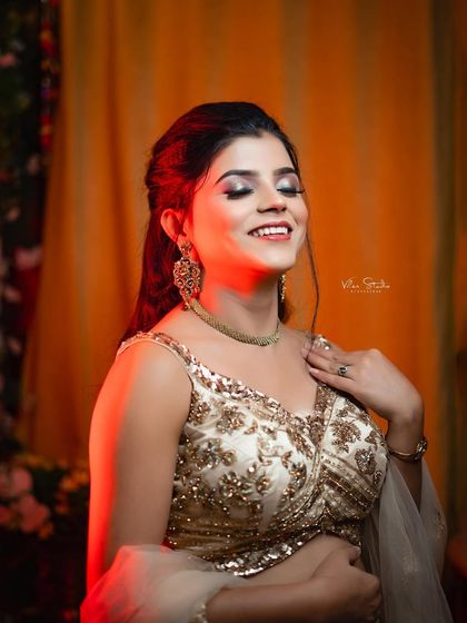 A joyful, candid moment of the bride with her eyes closed and a happy smile. The warm, colorful lighting adds to the celebratory feel of this pre-ceremony portrait.