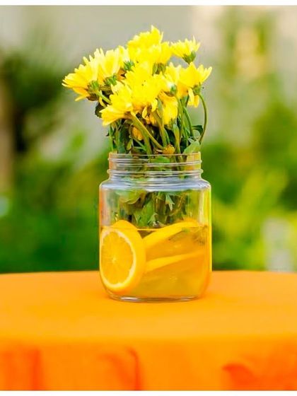 A simple yet elegant centrepiece. A mason jar with yellow flowers and orange slices sits on a bright orange tablecloth, adding a pop of colour to the guest tables.