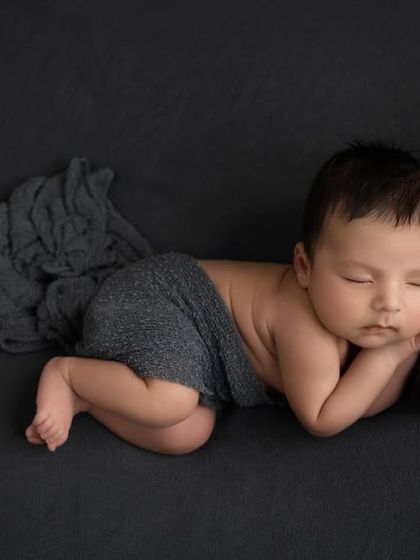 A variation of the pose on a grey backdrop, with the baby resting on a tiny matching pillow and partially covered by a soft wrap.