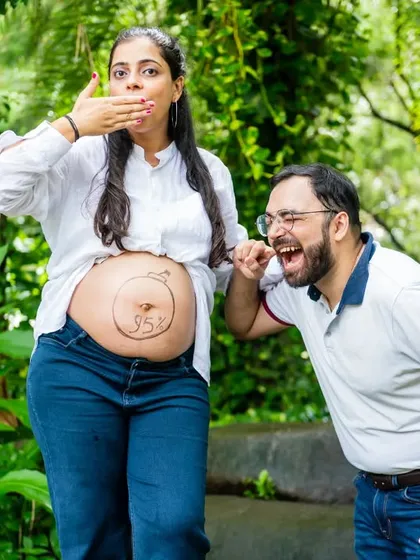 A playful and funny shot. The dad-to-be pretends to listen to the baby bump, which has "95%" written on it, capturing the fun side of pregnancy.