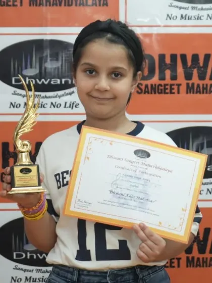 A young student proudly holds her certificate and trophy.