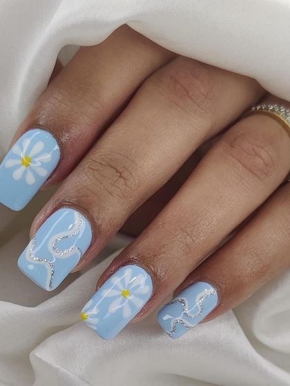 A cute and cheerful design on square nails, with hand-painted daisies and a silver glitter snake accent on a baby blue base.