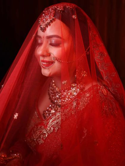 A dreamy shot of my bride under a red veil. The soft lighting highlights the glowing makeup and the intricate details of her bridal nath and jewellery.
