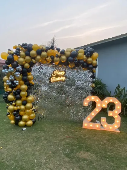 Celebrating a milestone birthday outdoors? This setup for a 23rd birthday features a shimmering silver sequin wall, a black and gold organic balloon garland, a custom neon sign, and large light-up marquee numbers.