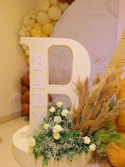 A large letter 'B' for "Baby" decorated with fresh white flowers and pampas grass. This detail from the Dior-inspired baby shower adds a natural and sophisticated touch.