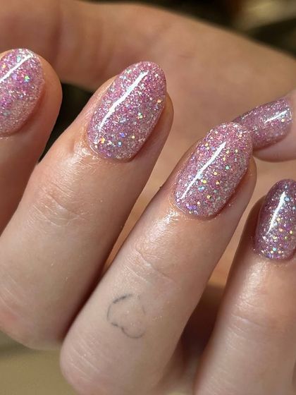 A close-up of a fun pink glitter polish. The mix of different sized glitter particles adds texture and a high-impact sparkle.