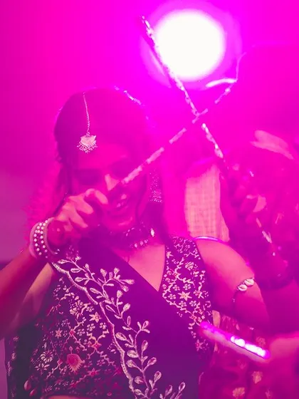 A dancer captured mid-twirl under the pink stage lights, dandiya sticks in motion. The energy on the dance floor during Navratri is truly special.