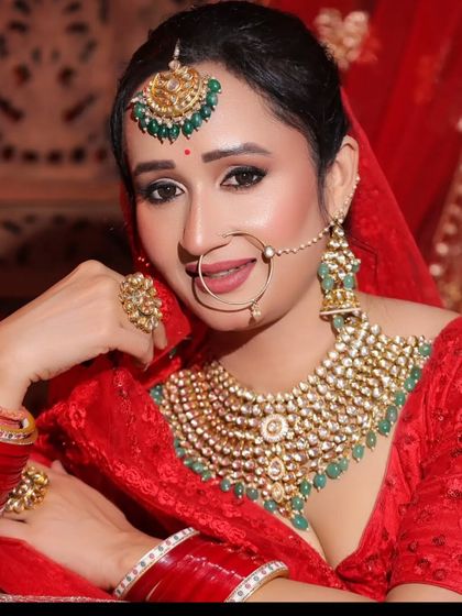 A beautiful bride in a red lehenga wearing a heavy Kundan choker with green beads. The oversized rings and nath complete the stunning look.