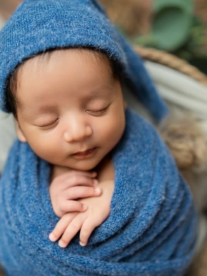 A close-up portrait of a baby wrapped snugly in a blue swaddle, with his tiny hands clasped together. This pose is all about comfort and serenity.