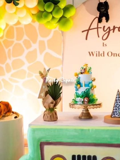 A close-up of the dessert table for Ayra's 'Wild One' party. The cake, props, and backdrop all feature a giraffe-print pattern and jungle foliage.