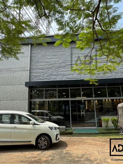 The entire exterior facade of this commercial building is covered in light grey PU stone panels. This gives the building a solid, monumental appearance while being a lightweight and practical cladding solution.