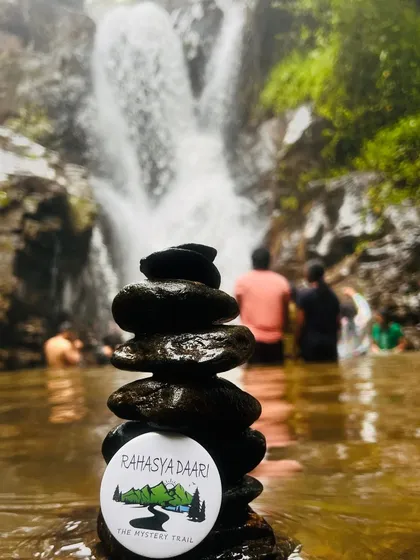 A creative shot of our Rahasya Daari badge balanced on a stack of pebbles in a waterfall pool.
