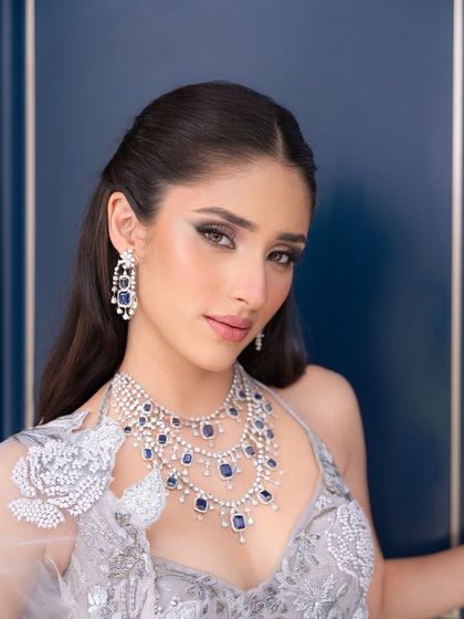 A close-up of the signature cocktail glam. The look features a defined eye, flawless skin, and a soft lip, perfectly framing her face and highlighting the stunning sapphire and diamond necklace.