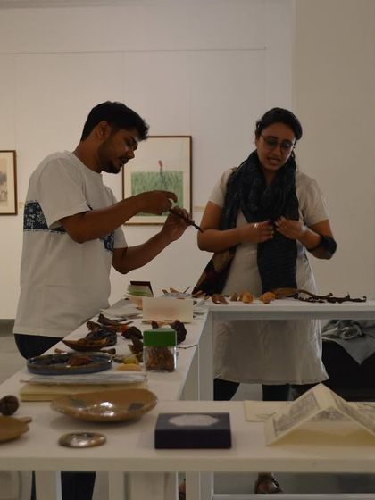 Artist Mohit Mahato and a visitor examining small, delicate objects on the installation table at 'Bring me Flowers'.