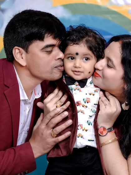 A sweet family portrait from a first birthday party. The parents shower their little one with kisses against a colorful rainbow backdrop, a perfect representation of a year filled with love.