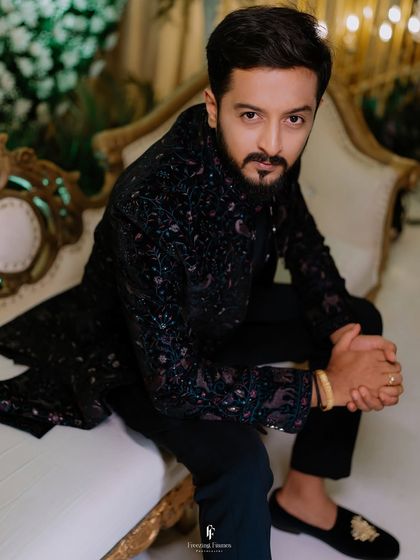 A portrait of the groom seated, looking directly at the camera with a confident and relaxed expression.