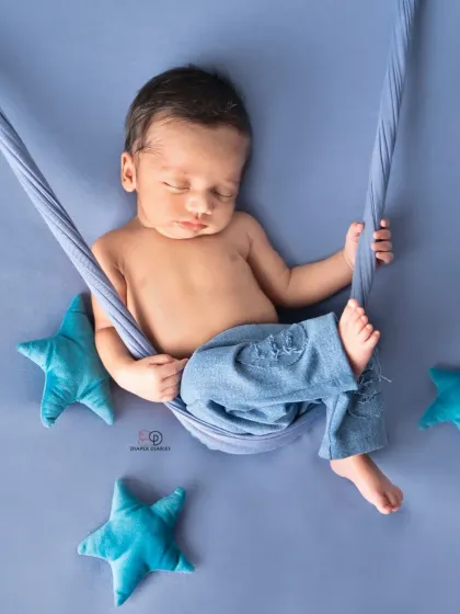 A newborn boy sleeps peacefully in a blue sling hammock, surrounded by plush blue stars. This simple setup creates a dreamy, celestial-themed newborn portrait.