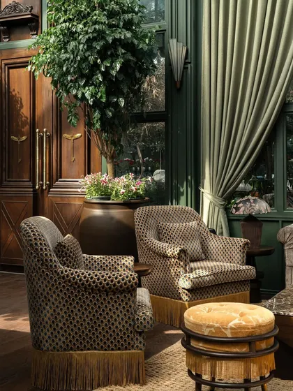 The foyer, where patterned armchairs and a large potted tree welcome guests into the space.