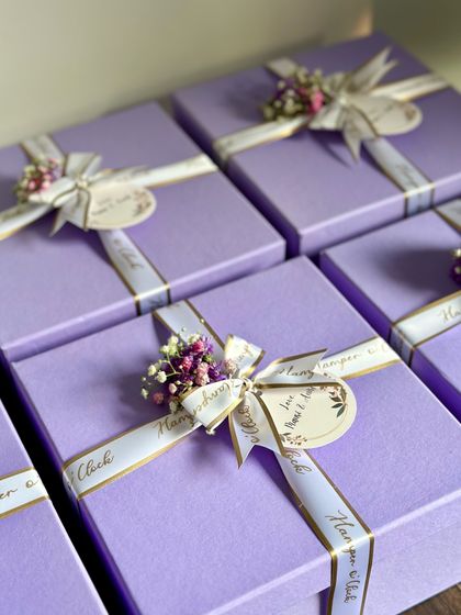 Elegant lavender boxes for a baby shower or first birthday celebration. Each box is tied with a custom "Hamper o' Clock" ribbon and adorned with a delicate dried flower bouquet, making for a very special return favor.