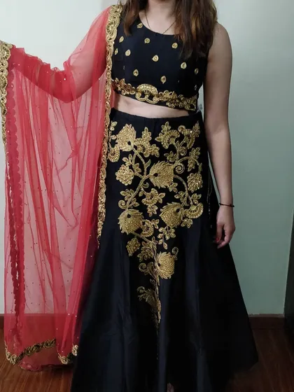 Our classic black lehenga paired with a bright red net dupatta offers a timeless look. The skirt features prominent gold floral embroidery, making it a versatile outfit for any evening wedding function or festive party.