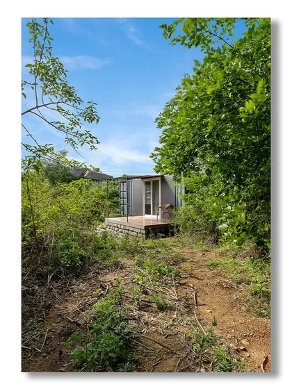 A view of 'The Boulder Nest' container home, nestled in a wild, natural landscape. This shot emphasizes its seclusion and eco-friendly ethos, blending modern living with untouched nature.