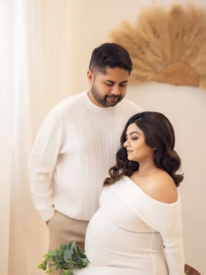 A tender moment from the cozy couple's session, with the mom-to-be seated and her partner standing protectively behind her.