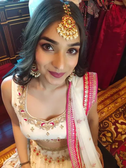 A stunning wedding guest ready for the ceremony. Her makeup features a soft brown smokey eye and a deep berry lip, paired with a traditional maang tikka for a festive touch.