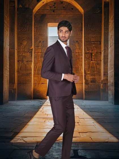 Walk into your wedding day with unmatched style. A model in a deep purple suit, set against a dramatic, ancient-themed backdrop.