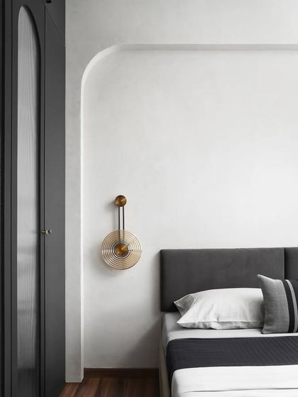 A round, fluted wall light casts a warm glow, contrasting beautifully with the cool, monochrome theme of this bedroom. The arched wall detail adds a soft, architectural element.