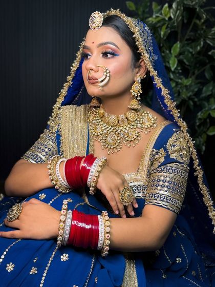 A seated portrait of a Rajputi bride in a royal blue lehenga. The makeup features a pop of blue eyeliner to match the outfit, creating a cohesive and stunning look.