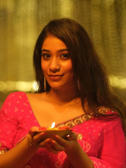 A close-up portrait, her face lit by the diya she holds. The soft light creates an intimate and serene mood, celebrating the festival of lights.