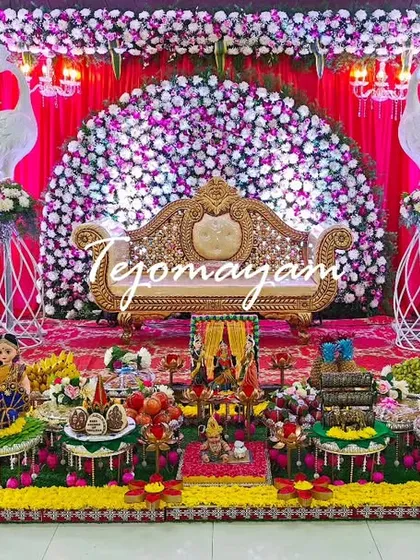 A beautiful baby shower setup featuring a backdrop of cascading flowers and peacock figures. The arrangement of traditional plates on the stage is both colorful and elegant.