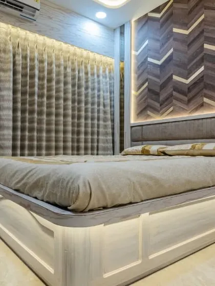 This bedroom in Mahad features a striking chevron-patterned wood headboard wall with integrated lighting. The floating bed design enhances the modern aesthetic and makes the room feel more spacious.