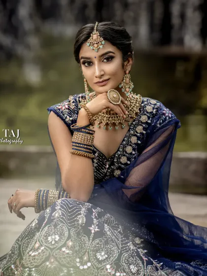 A classic seated bridal portrait in a beautiful blue lehenga. The outdoor setting and her poised expression create a look of timeless elegance.