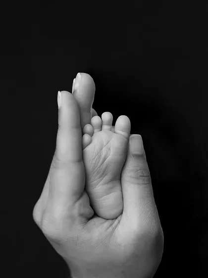 A baby's foot held in their parent's hand, captured in beautiful black and white. This artistic shot focuses on the form and texture of this tiny detail.