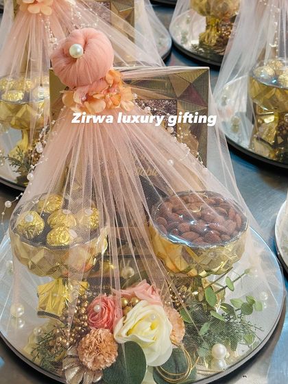A multi-tiered hamper is a fantastic way to present a variety of gifts. This one, wrapped in delicate net, holds bowls of Ferrero Rocher and almonds, making it a truly impressive wedding gift.