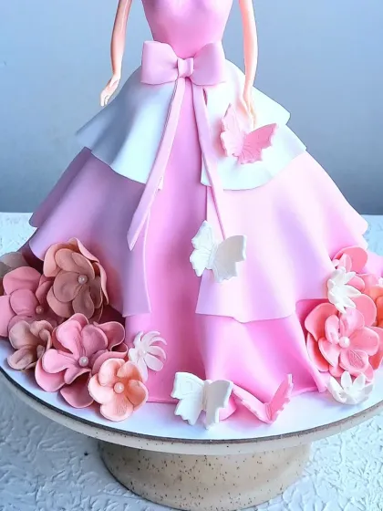 A close-up of the Barbie doll cake, showing the layered fondant dress and the arrangement of sugar flowers and butterflies.