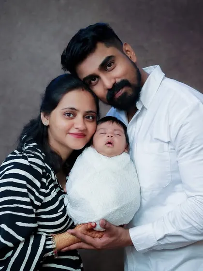 A beautiful first family portrait. The parents are looking at the camera, proudly presenting their swaddled newborn. This is a classic shot that every new family wants to have.